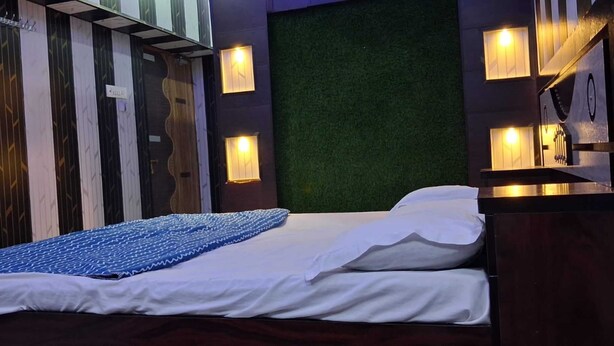 A single bed with a blue patterned bedspread, a white pillow, and a green wall behind it. - Gopalkunj Homestay (Faizabad)