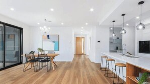 A modern kitchen with a central island, bar stools, and pendant lighting. - Modern Luxe Haven – Your Geelong Escape (Highton)