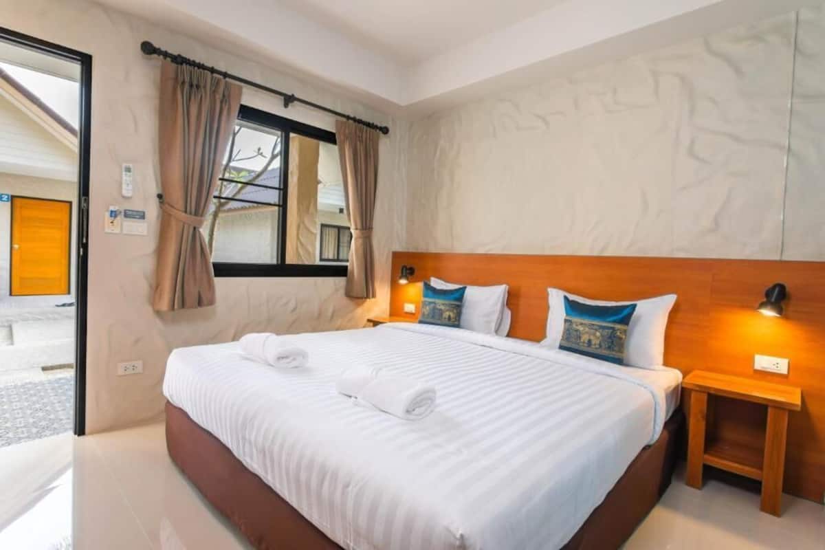 Habitación de hotel con una cama grande, una mesita de noche, una ventana con cortinas y una pared con diseño texturizado.