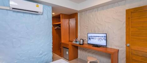 A hotel room with a bed, a desk with a television, a wardrobe, and an air conditioning unit.