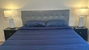 Un letto con testiera trapuntata, due comodini con lampade e una parete liscia.