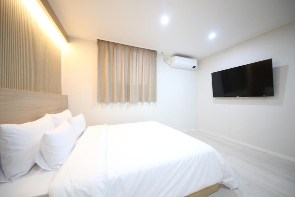 A hotel room with a bed, a mounted TV, and an air conditioning unit.