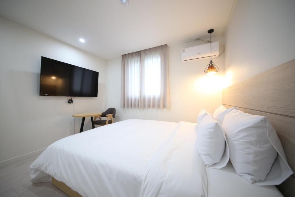 Habitació d'hotel amb un llit, un televisor fixat a la paret, un escriptori amb una cadira i una finestra amb cortines.