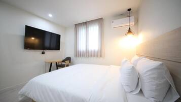Habitació d'hotel amb un llit, un televisor fixat a la paret, un escriptori amb una cadira i una finestra amb cortines.