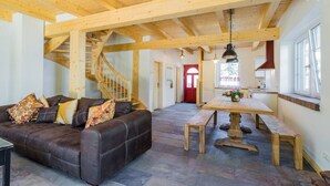A spacious living area with a leather sofa, wooden beams, a staircase, a dining table, and a kitchen area. - Nature experience & close to the city of Berlin: "THE WELSH HOUSE" (No. 56a) (Schönwalde-Glien)