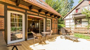 A wooden deck with wicker chairs and a table, a covered patio area, and a view of a forested area. - Nature experience & close to the city of Berlin: "THE WELSH HOUSE" (No. 56a) (Schönwalde-Glien)