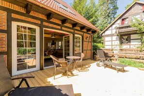 A wooden deck with wicker chairs and a table, a covered patio area, and a view of a forested area. - Nature experience & close to the city of Berlin: "THE WELSH HOUSE" (No. 56a) (Schönwalde-Glien)