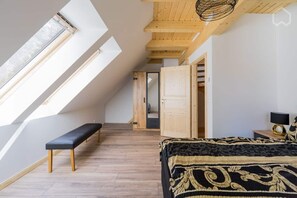 A bedroom with a sloped ceiling, skylight, wooden flooring, a bench, a bed with a patterned bedspread, and a nightstand with a lamp. - Nature experience & close to the city of Berlin: "THE WELSH HOUSE" (No. 56a) (Schönwalde-Glien)