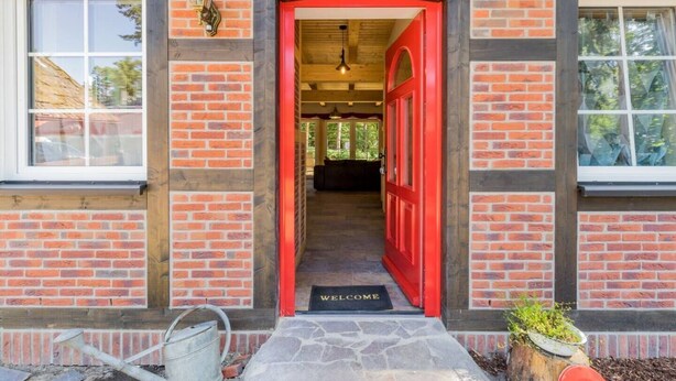 A red door with a 'WELCOME' mat, a brick exterior, and a window on the left. - Nature experience & close to the city of Berlin: "THE WELSH HOUSE" (No. 56a) (Schönwalde-Glien)