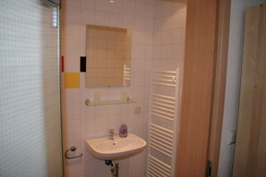 Ein Badezimmer mit einem weißen Waschbecken, einem Spiegel, einem Handtuchhalter und einer Duschkabine.