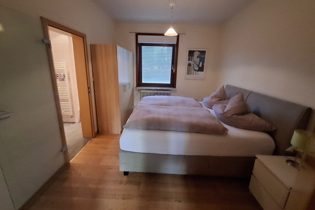 Ein Schlafzimmer mit Bett, Nachttisch, Kleiderschrank und einem Fenster mit Jalousien.