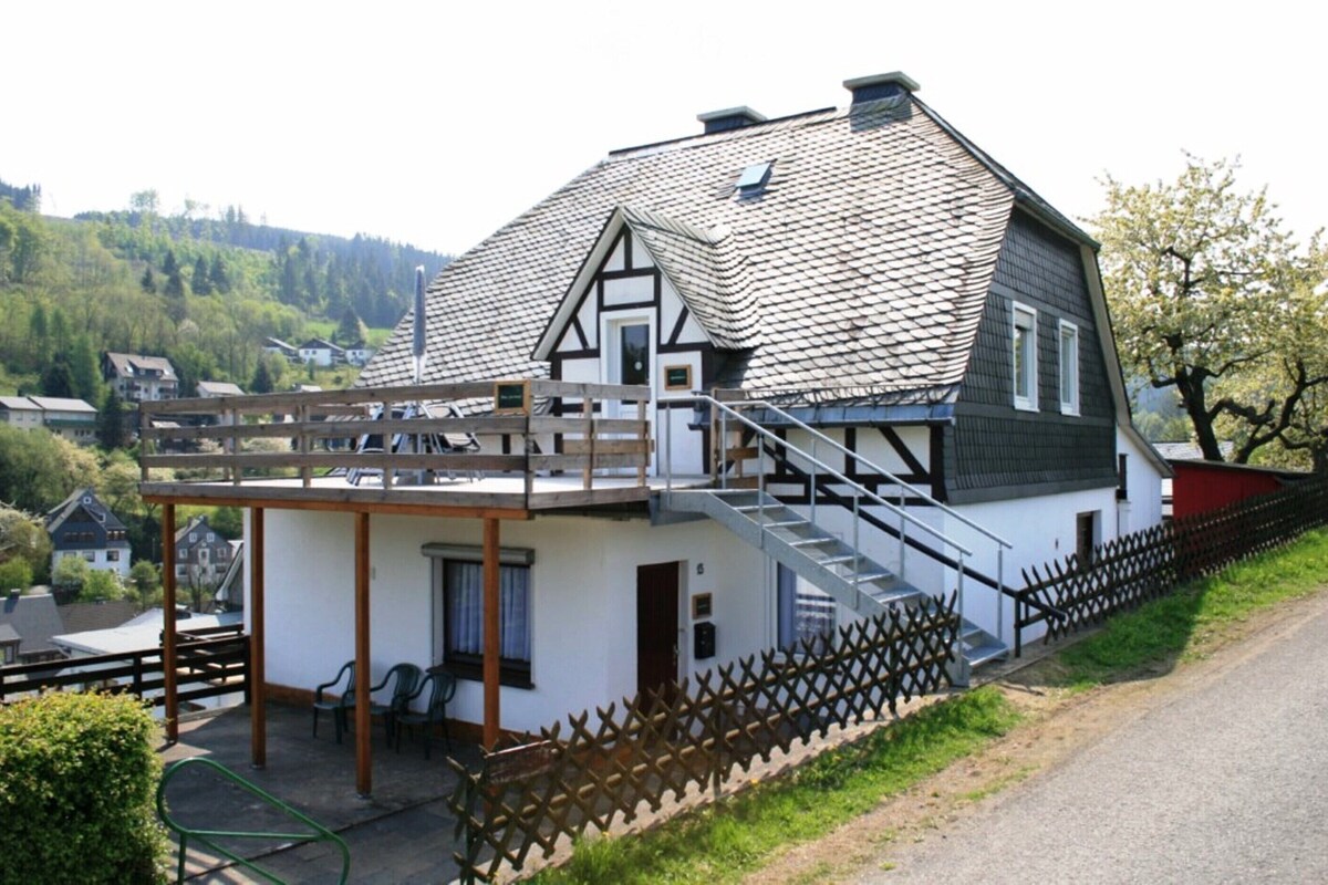 Ein traditionelles Chalet mit steilem Dach, einer Holztreppe und einem umzäunten Außenbereich.