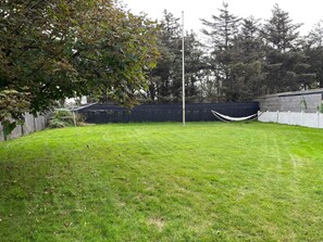 A grassy backyard with a hammock, a wooden fence, and trees in the background. - 4 Star Holiday Home in Lokken (Lokken)