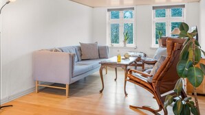 A room with a light-colored sofa, a wooden coffee table, a wicker chair, and a large plant. - 4 Star Holiday Home in Lokken (Lokken)