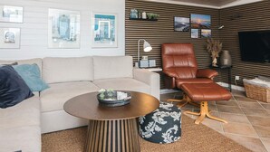 A modern living room with a sofa, a brown leather chair, a round coffee table, and a flat-screen TV mounted on the wall. - 4 Star Holiday Home in Hejls (Hejls)