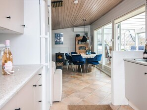 A modern kitchen with white cabinets, a dining area with blue chairs, and a large window providing natural light. - 4 Star Holiday Home in Hejls (Hejls)