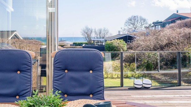 A wooden deck with two chairs, woven placemats, and a potted plant. - 4 Star Holiday Home in Hejls (Hejls)