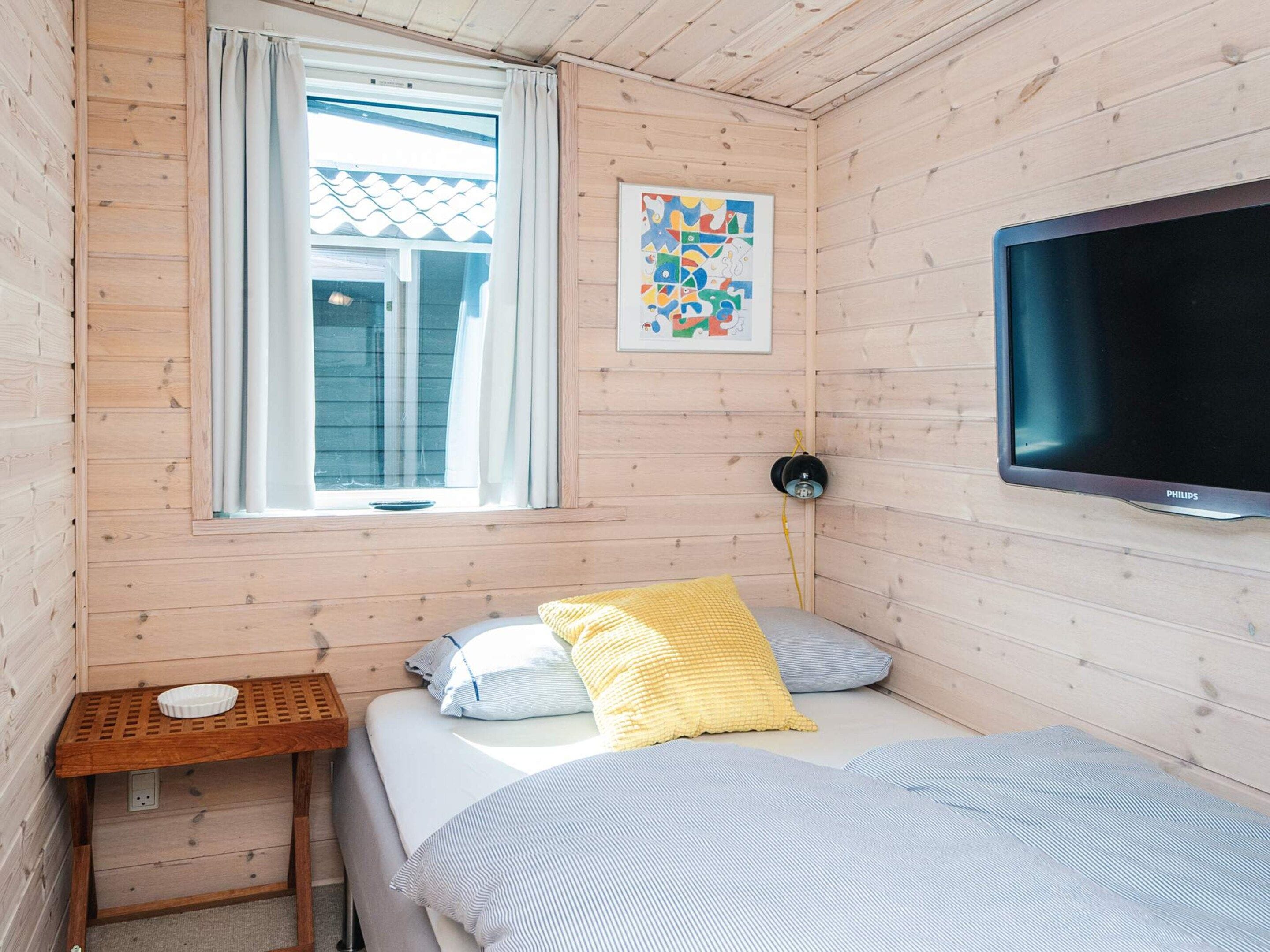 A small room with a bed, a TV, a window, and a wall-mounted artwork.