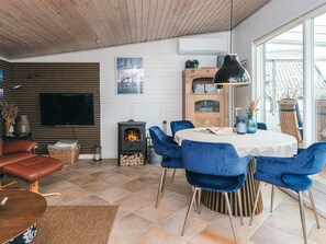 A modern living room with a fireplace, a dining table, blue chairs, and a television. - 4 Star Holiday Home in Hejls (Hejls)