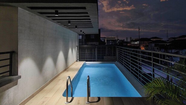 A rooftop pool with a metal railing, a concrete wall, and a view of the city skyline at dusk. - Mildy Lodge And Apartment  (Abuja)