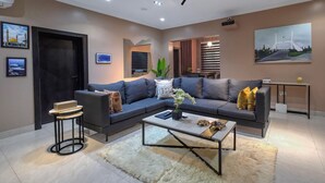 A modern living room with a sectional sofa, a coffee table, a small side table, and a TV. - Mildy Lodge And Apartment  (Abuja)