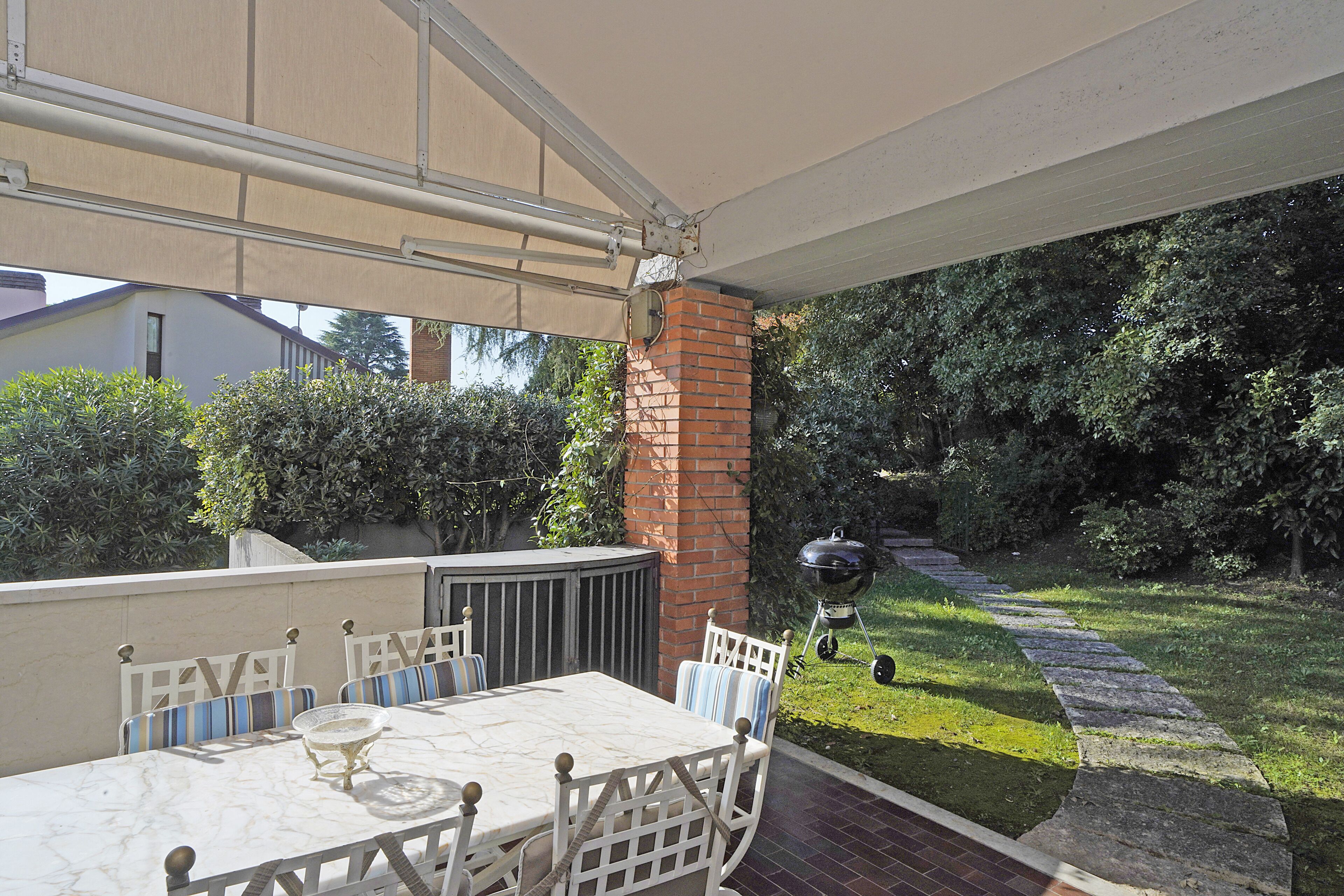 An outdoor patio with a table and chairs, a barbecue grill, and a brick wall.