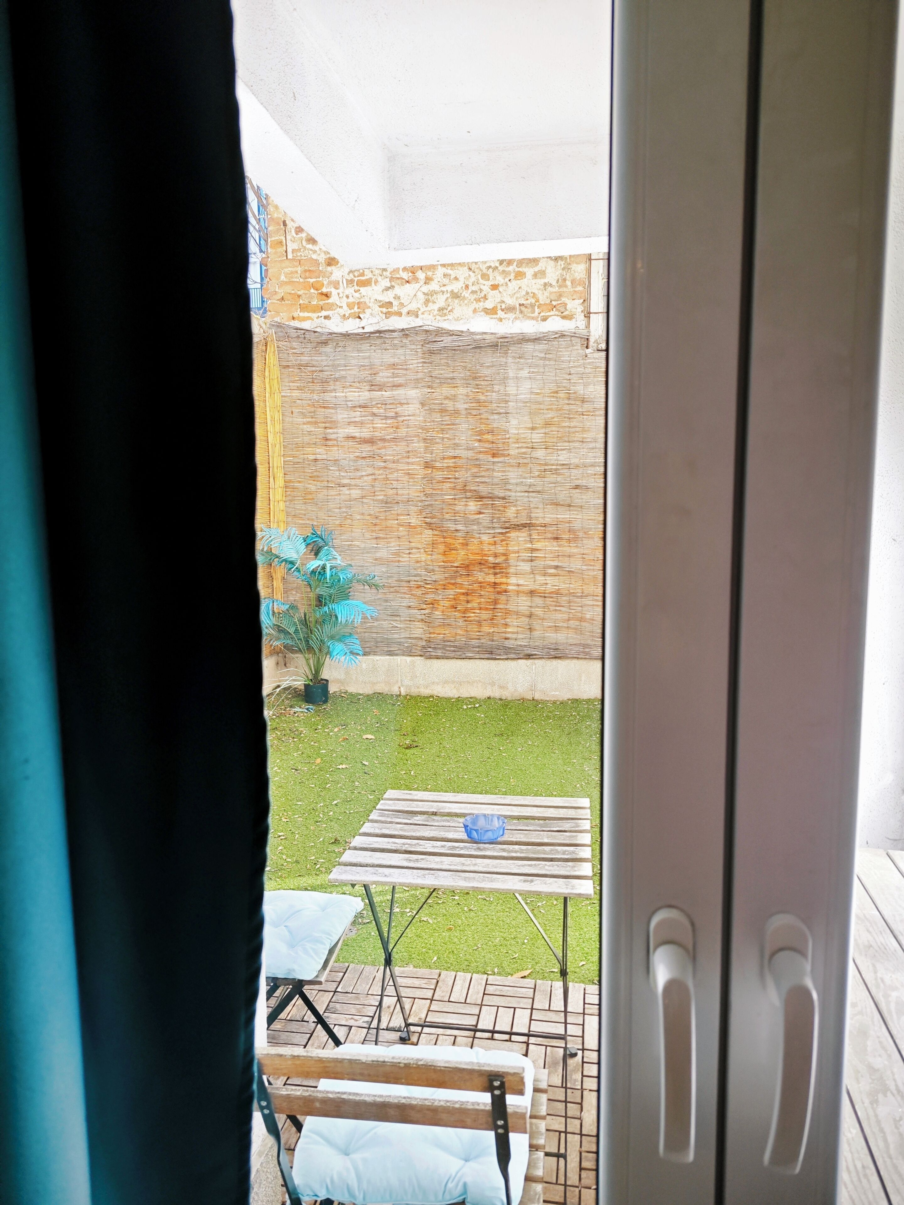 A view through a doorway into a room with a wooden table and a bench, a small potted plant, and a brick wall.