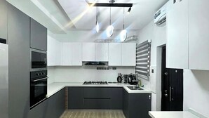 A modern kitchen with a central island, built-in appliances, and pendant lighting. - House 21 Hotel (Asaba)