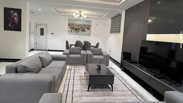 A modern living room with grey sofas, a coffee table, and a flat-screen TV. - House 21 Hotel (Asaba)