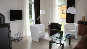 Ein modernes Wohnzimmer mit Flachbildfernseher, zwei Sessel, einem Glastisch und einer Lampe.