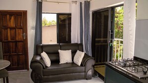 Un salon comprenant un canapé, une table à manger, un coin cuisine avec une cuisinière et une porte-fenêtre coulissante donnant sur un balcon.