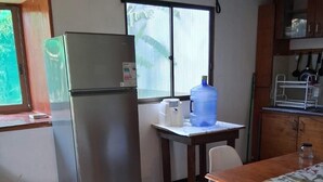 Une cuisine compacte équipée d’un réfrigérateur, d’un distributeur d’eau, d’une fenêtre et d’un coin repas avec des chaises.