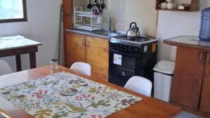 Une cuisine compacte avec des meubles en bois, une cuisinière à gaz, une bouilloire et une table à manger avec des chaises.