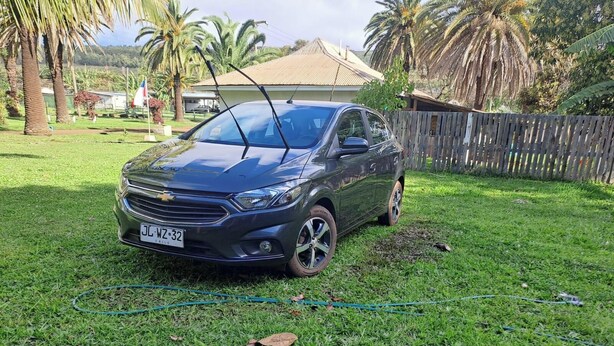 Une voiture est garée sur une pelouse, avec une clôture en bois et des palmiers en arrière-plan.