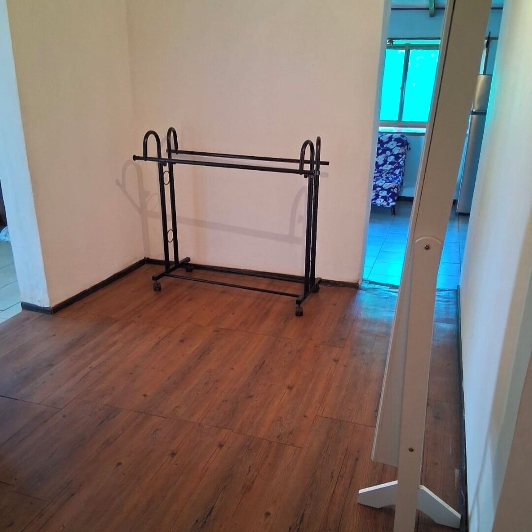 Una stanza d'angolo con pavimento in legno, un portaropi in metallo e una porta che dà su un'altra stanza.