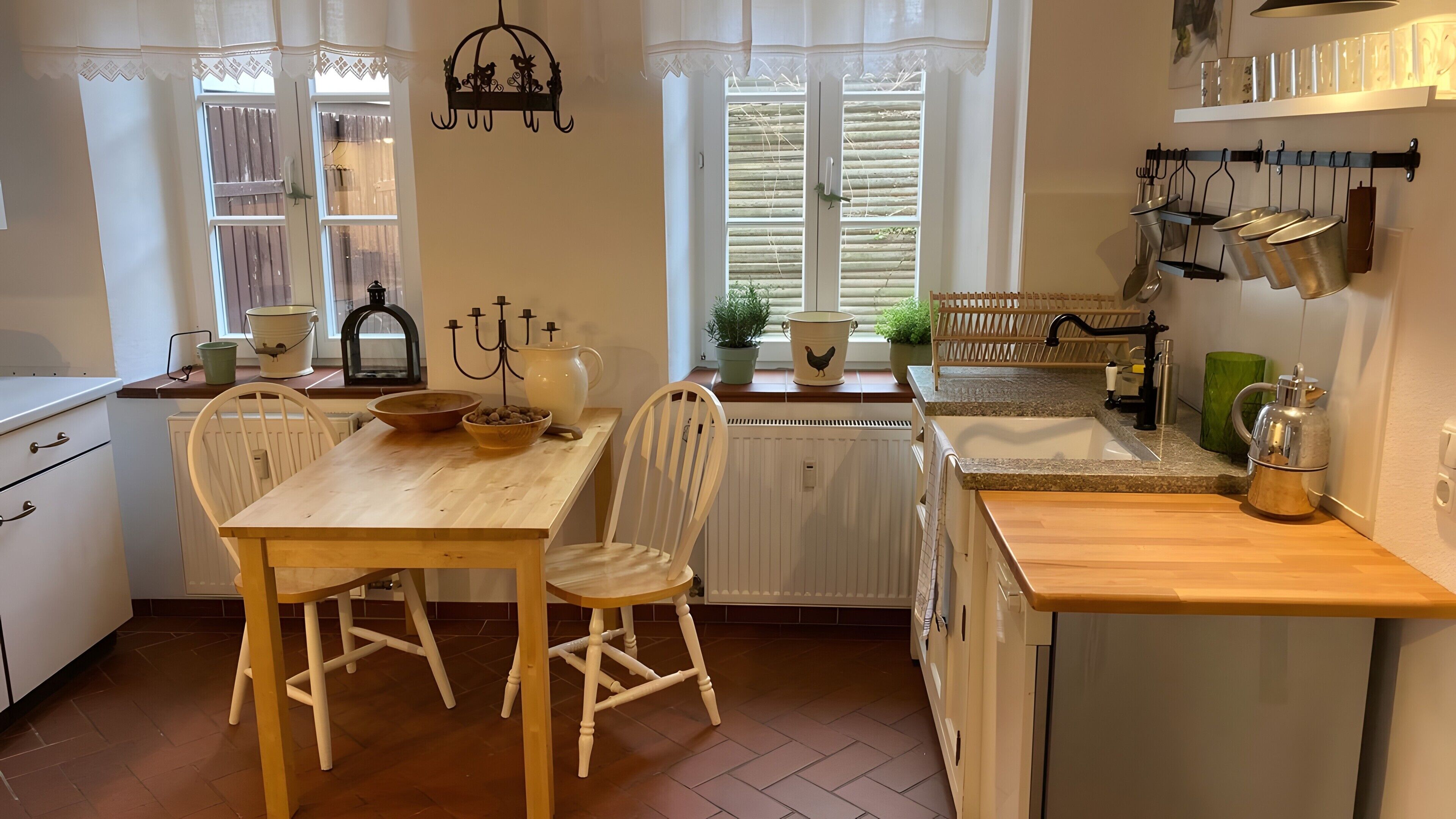 A kitchen with a wooden table, chairs, a radiator, a sink, and various kitchen utensils.