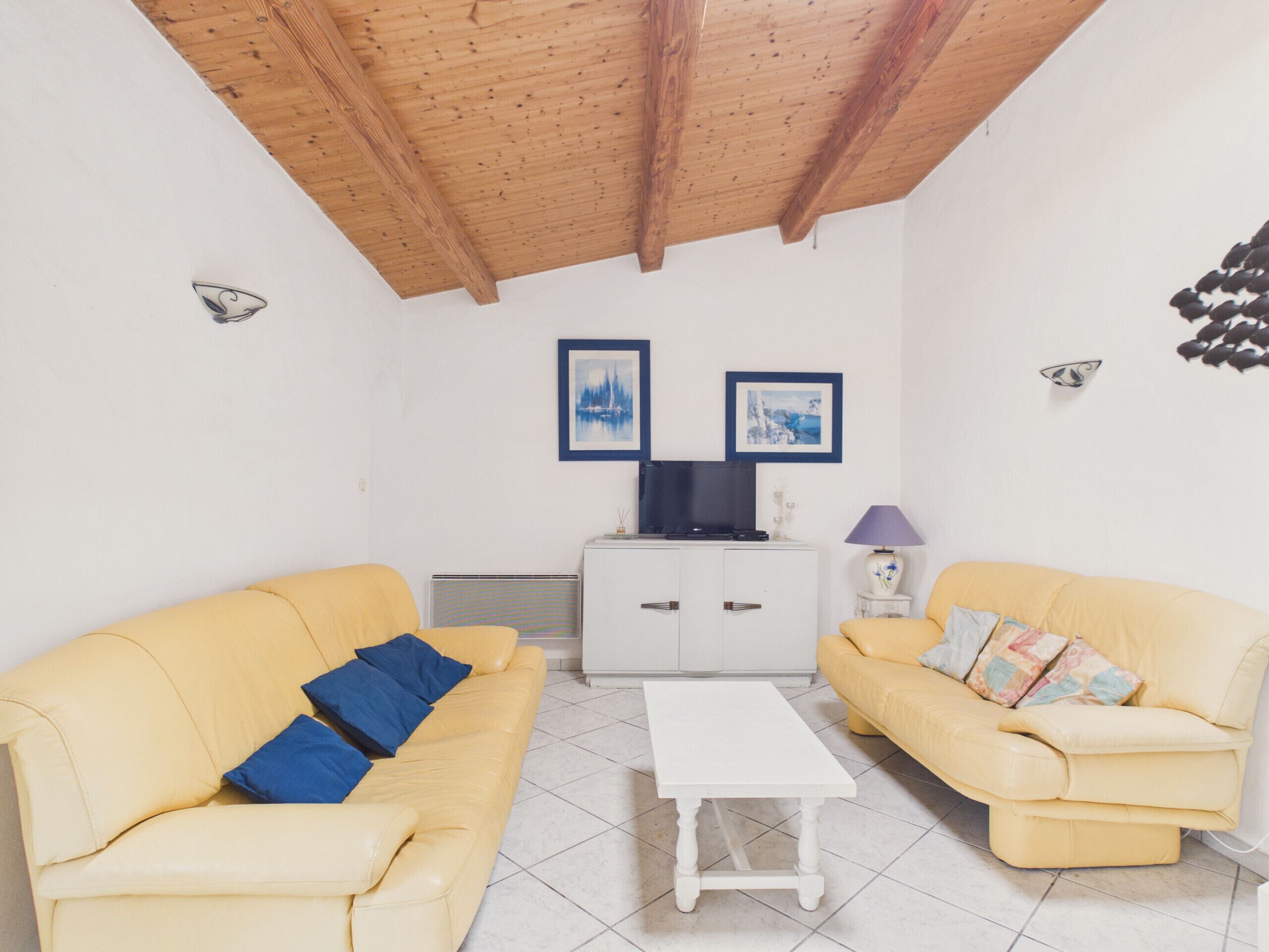 A living room with two yellow sofas, a white coffee table, a TV on a cabinet, and framed pictures on the wall.