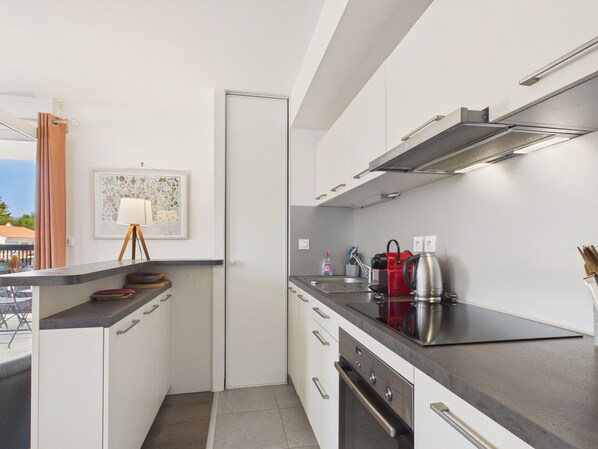 A modern kitchen with white cabinets, a stainless steel range hood, a red kettle, and a small sink. - Apartment in the heart of Les Sables for 4 (Les Sables-d´Olonne)