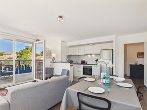 Eine moderne Küche mit weißen Schränken, einem Essplatz für zwei Personen und einem Balkon mit Blick auf Häuser und Bäume.