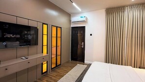 A modern hotel room with a large bed, a flat-screen TV, a wardrobe, and an air conditioning unit. - House-19 Apartments (Abuja)