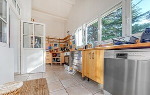A kitchen with wooden cabinets, a dishwasher, a stove, and a window overlooking greenery. - Charmante maison avec piscine (Saint-Palais-sur-Mer)