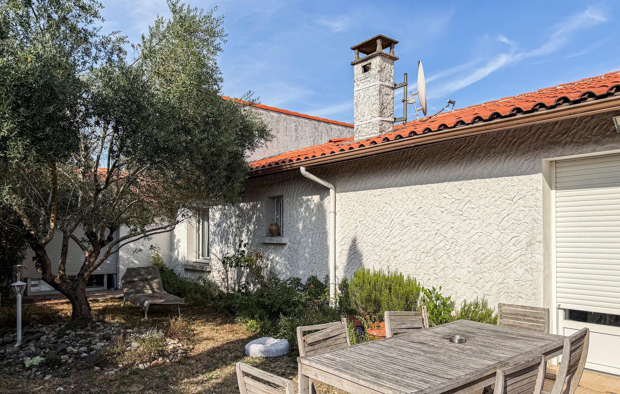 Il s’agit d’un bâtiment à l’extérieur en pierre, avec un toit en tuiles et une cheminée. On peut voir une table et des chaises à l’extérieur, ainsi qu’un arbre.