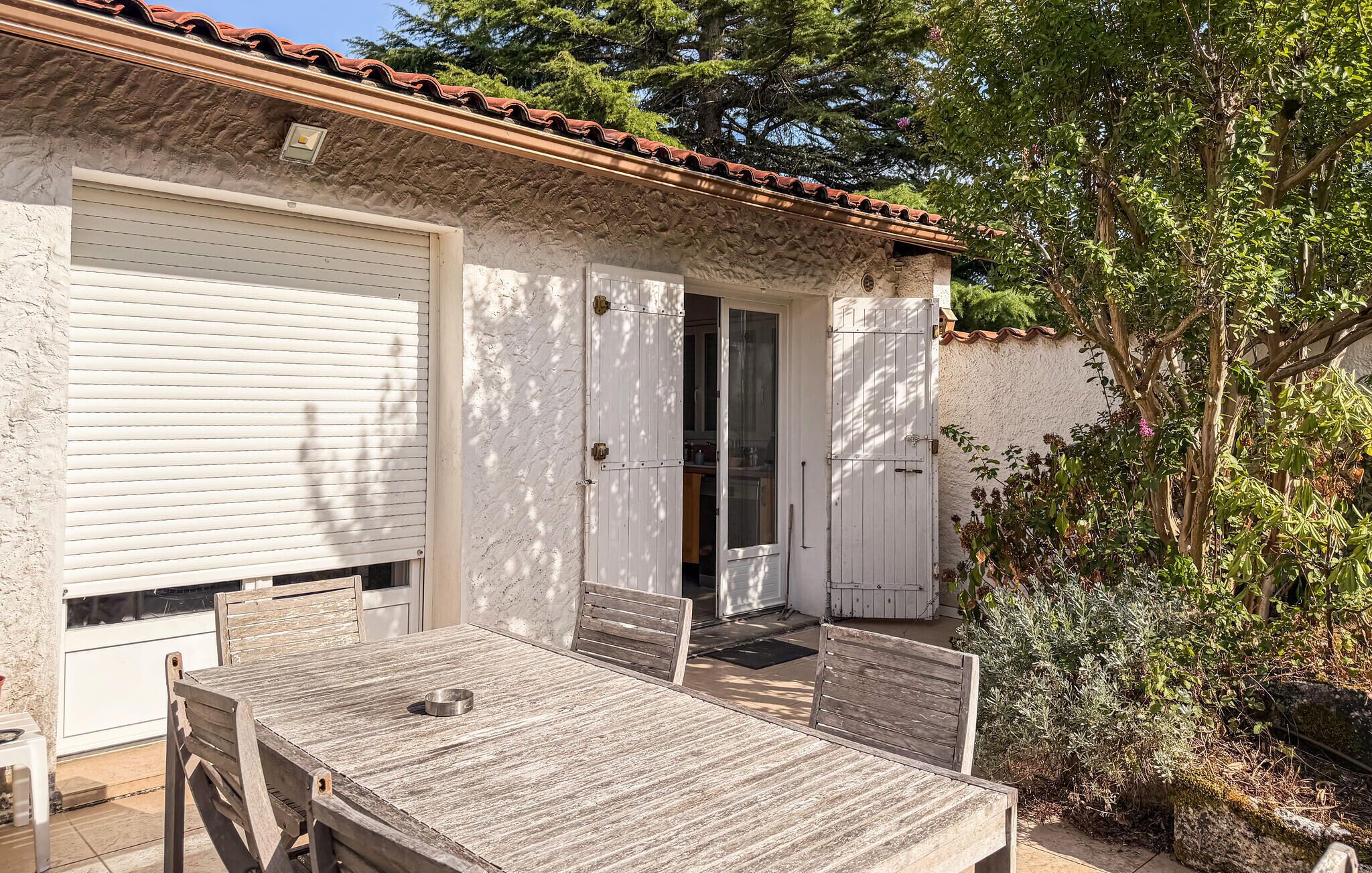 A patio with a wooden table and chairs, a white garage door, and a door leading to a covered area.