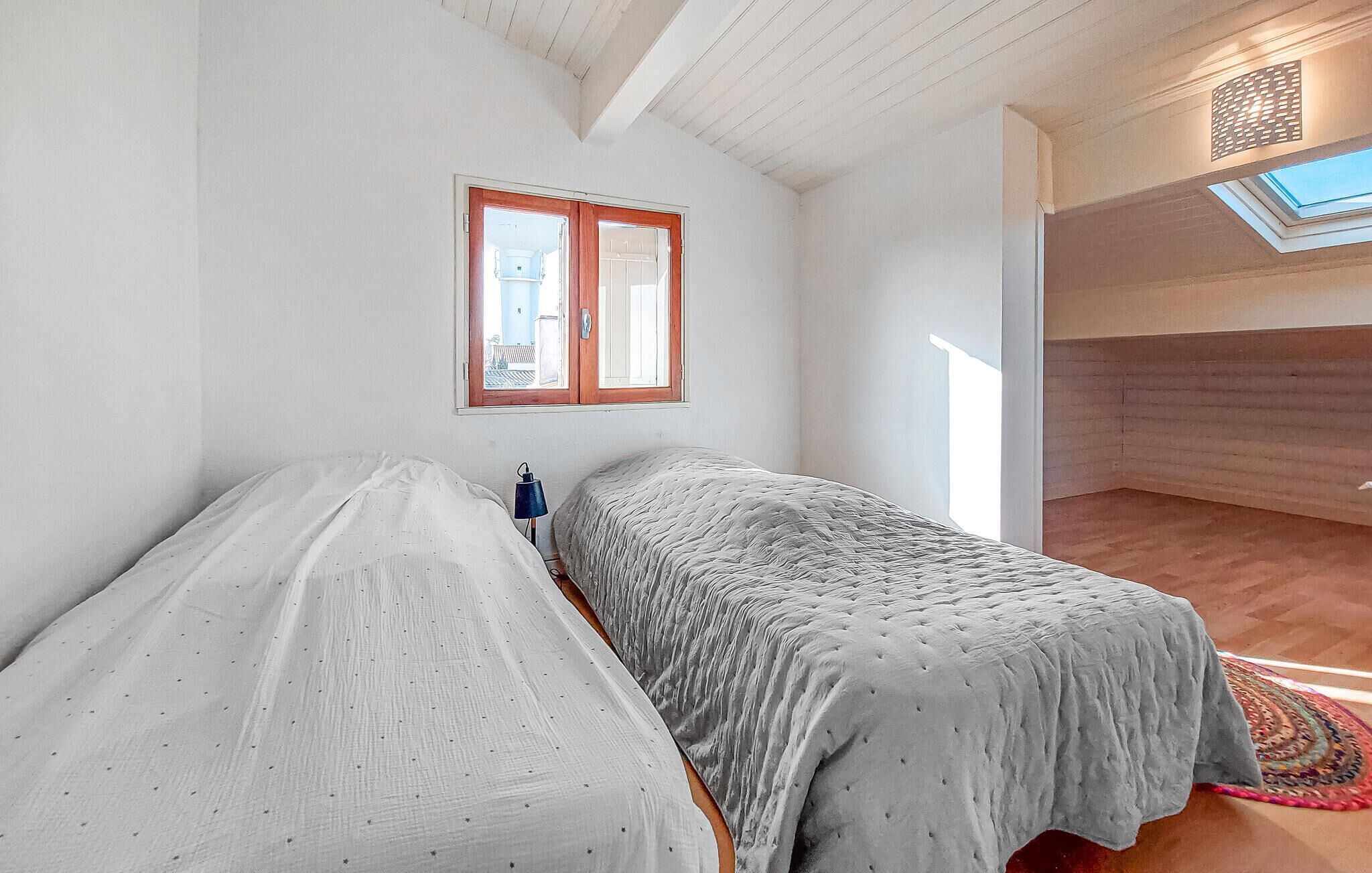 A bedroom with two beds, a skylight, and a view of the outside.