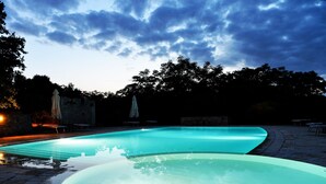 Ein Pool mit geschwungener Kante, umgeben von Steinplatten und beschattet durch Sonnenschirme.