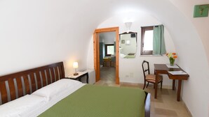 Ein Schlafzimmer mit Bett, Schreibtisch, Stuhl, Spiegel und einem kleinen Tisch mit Blumen.