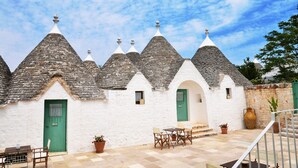 A building with conical roofs, a green door, and a patio with a table and chairs. - Room 'Corte Del Camedrio Lamia 2' with Shared Terrace, Wi-Fi and Air Conditioning (Ostuni)