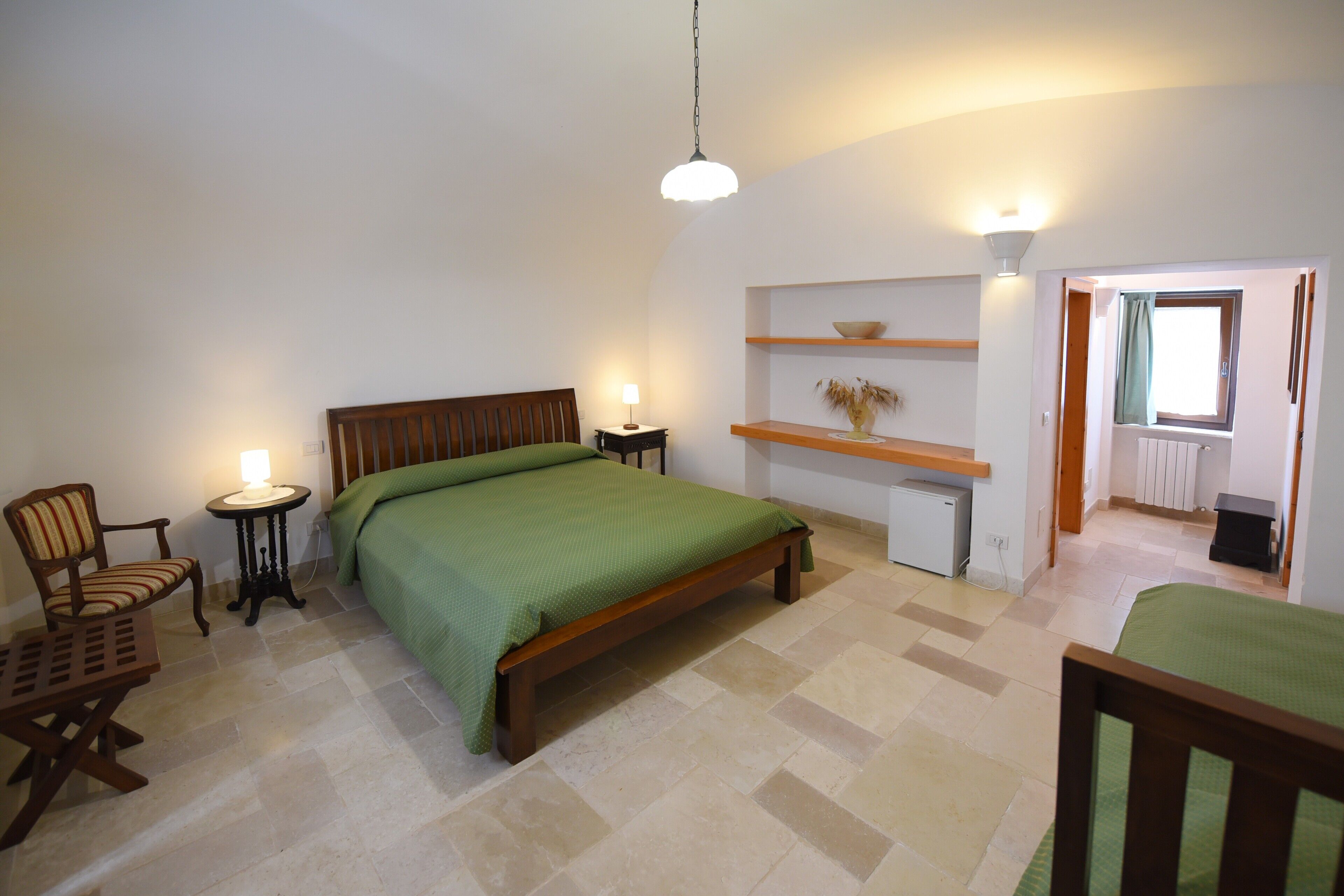 Ein Schlafzimmer mit Bett, Stuhl, einem kleinen Tisch, einer Ablage mit einer Vase und einem Fenster.