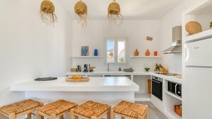 Eine moderne Küche mit einer zentralen Kochinsel, Barhocker, hängenden Korblichter und eingebauten Geräten.
