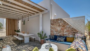 Ein moderner Außenbereich zum Sitzen mit einer Steinsäule, einer Holzpergola und einem weißen Tisch mit einer Bank.